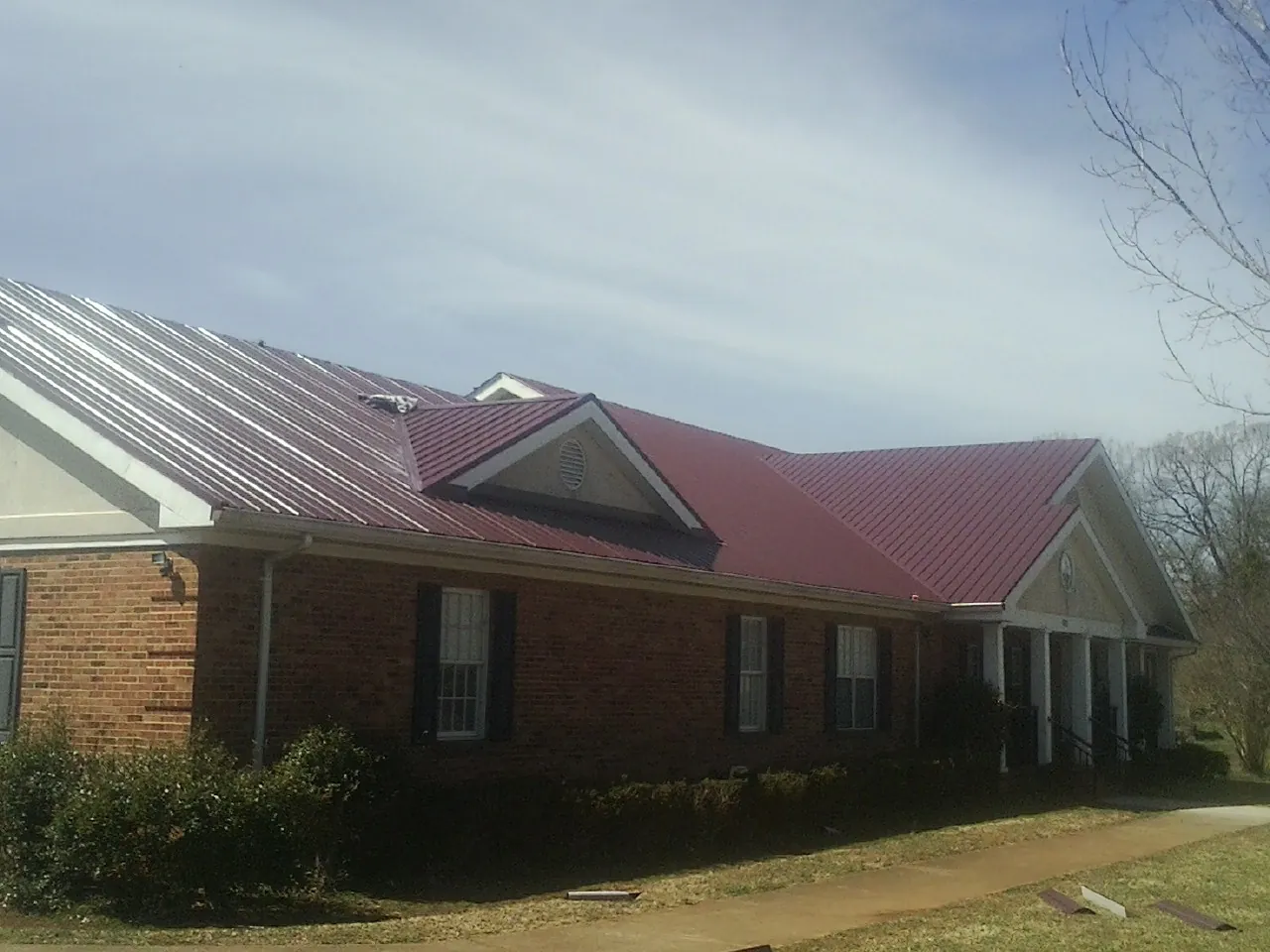 Red metal roof with gabled entries on a long brick building, from a Hail Damage Roof Repair job in Delaware