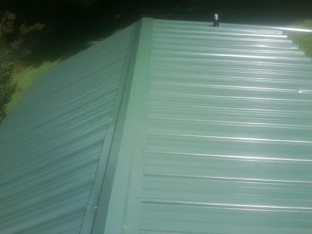 New green metal panels meeting at the ridge of a roof — Flat Roof Repair work by our crew in Delaware